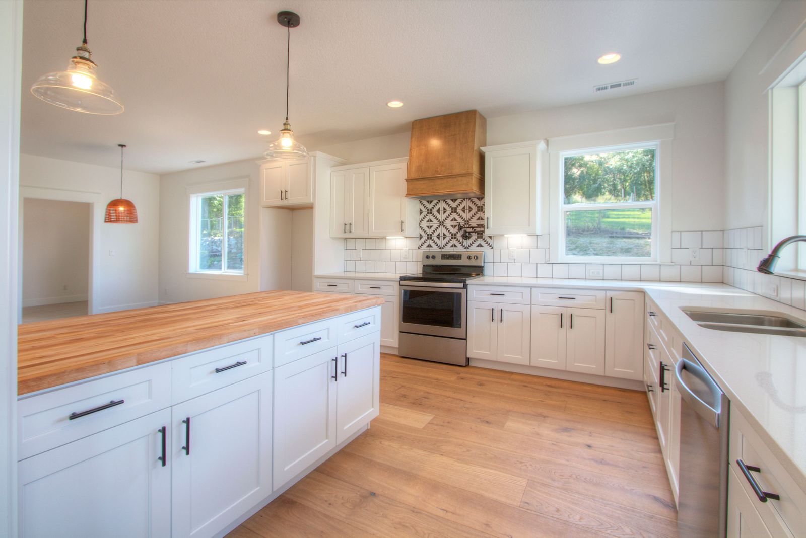 Remodeled farmhouse kitchen with white shaker cabinets, wood hood, and butcher block island by R Homes